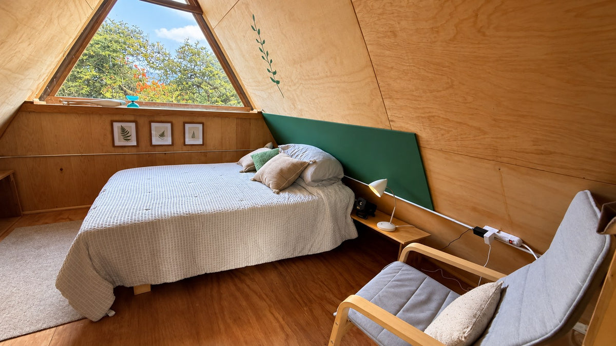 Interior de la Alpina A-Frame de BikiniHouses en Tapalpa, con cama y ventana hacia los árboles
